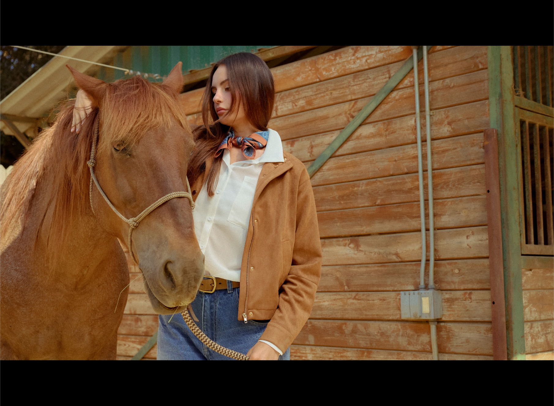 A person standing next to a horse in front of a wooden barn.