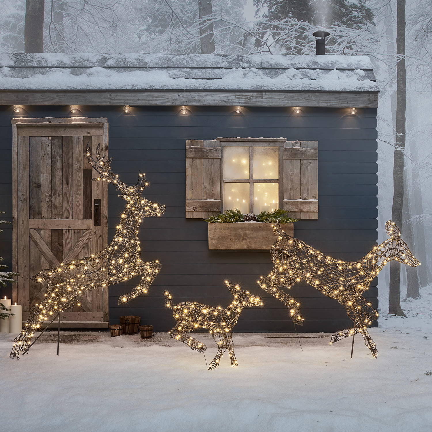 Rattan light up reindeer family in a snowy setting outside a winter cabin.