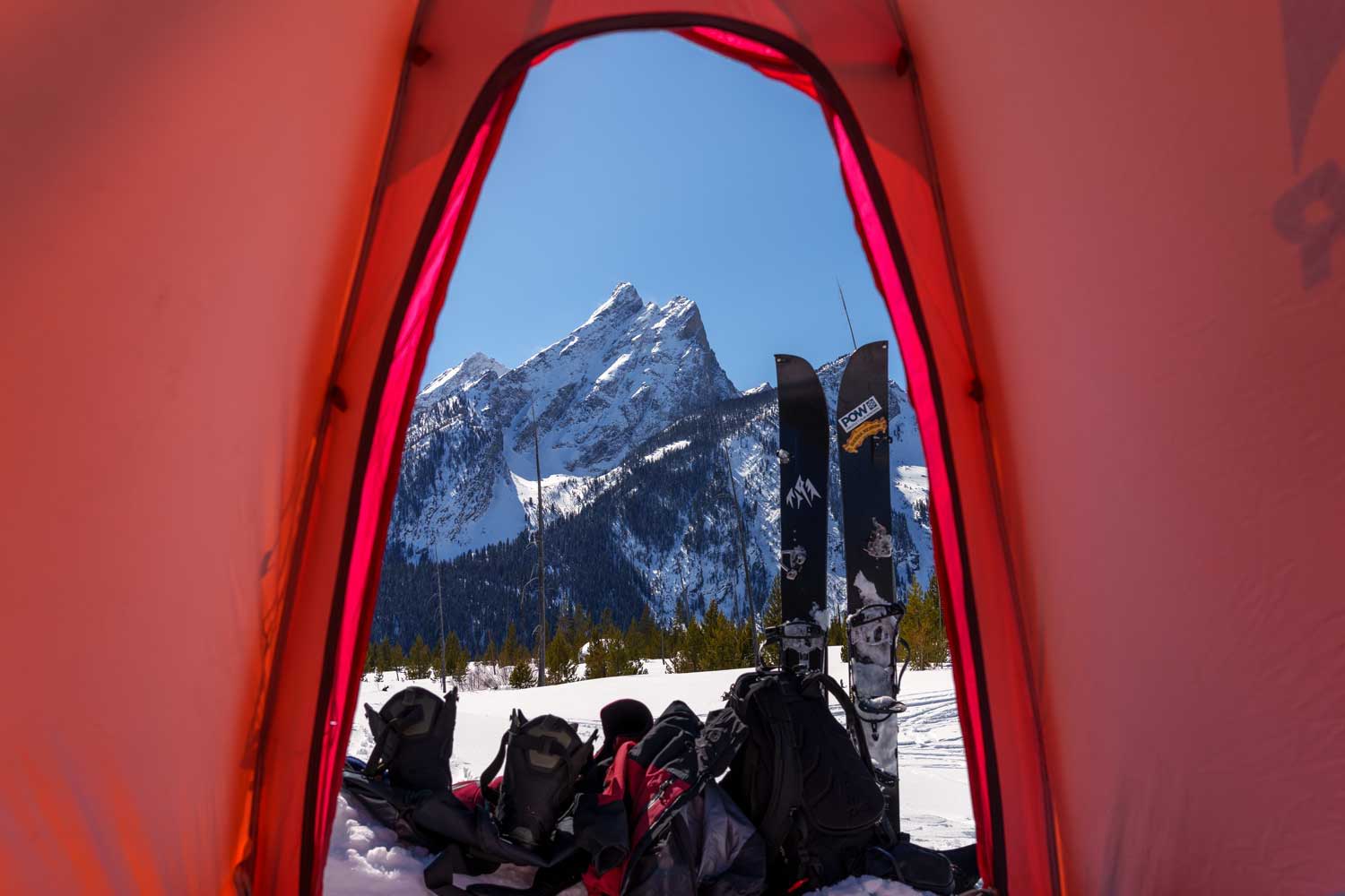 View of mountains and splitboard gear through a tent opening.