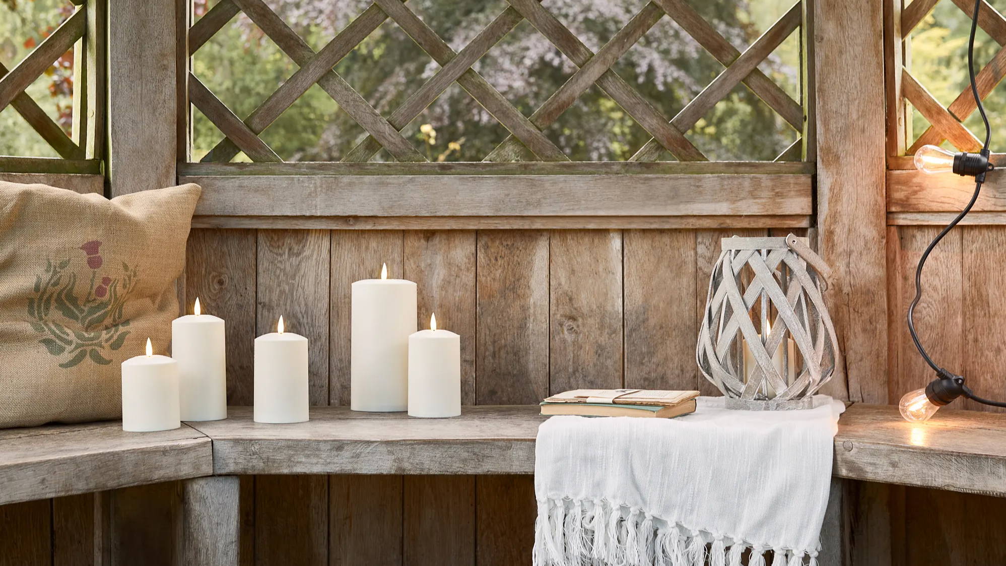 Summerhouse with TruGlow candles, woven garden lantern and festoons displayed on bench