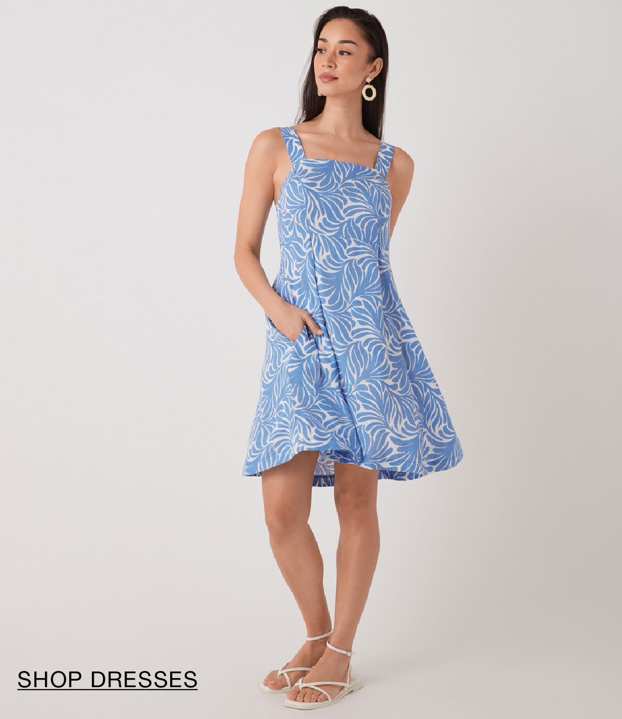 Woman in a blue floral dress with pockets, standing against a neutral background.