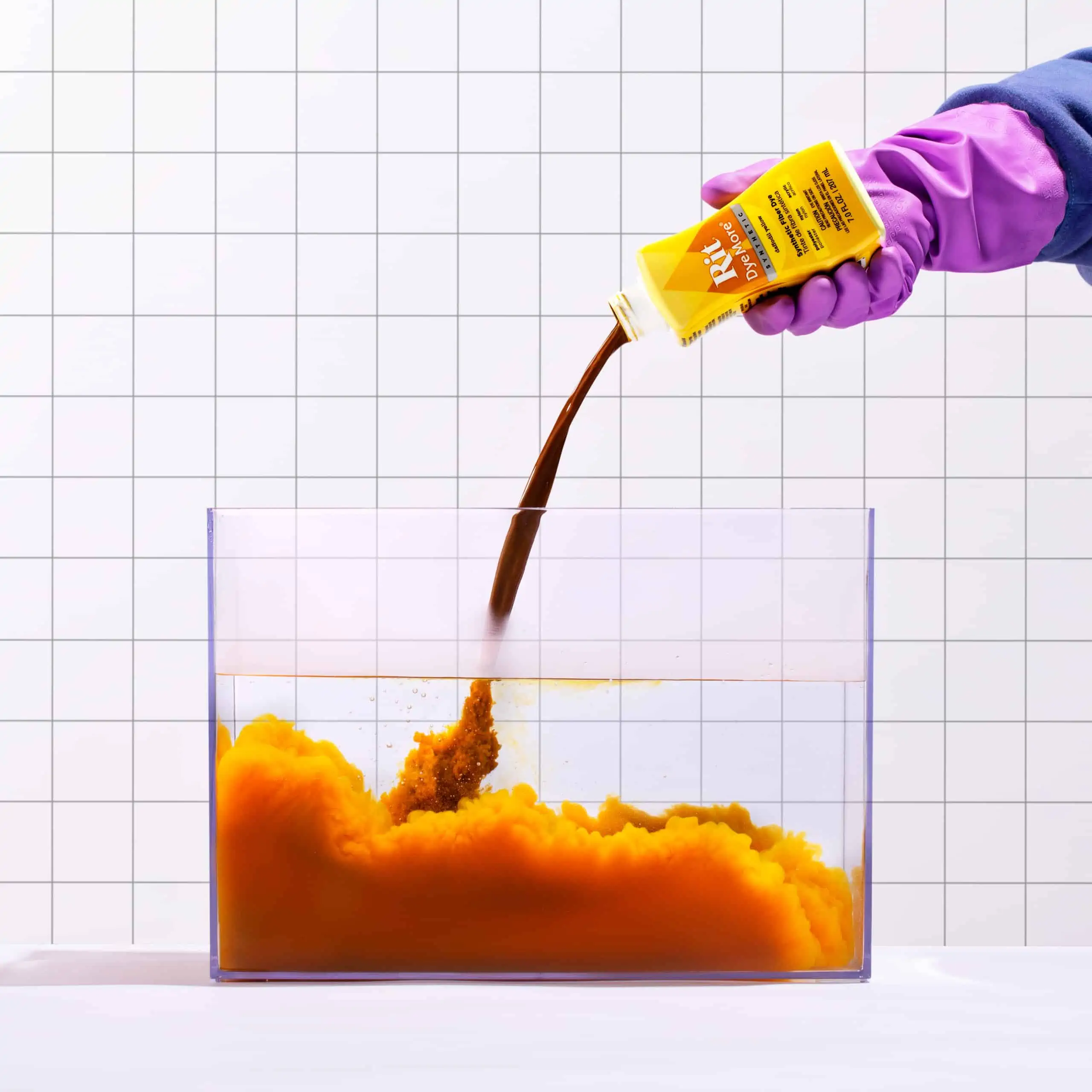 A gloved hand pours liquid into a container filled with orange substance.