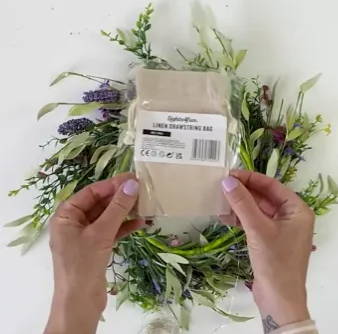A person holding a neutral linen bag in front of her spring wreath.