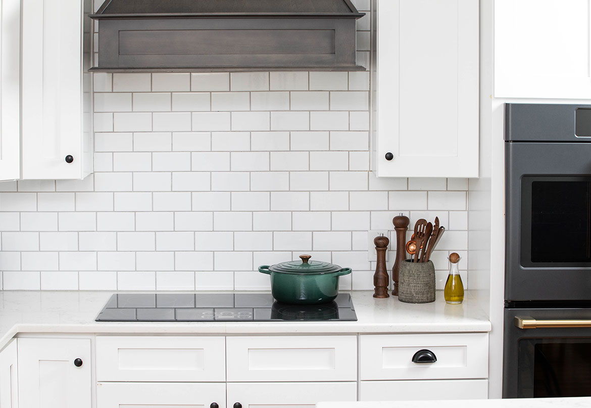 Induction cooktop with white cabinets, stovetop, green pot, and cooking utensils.