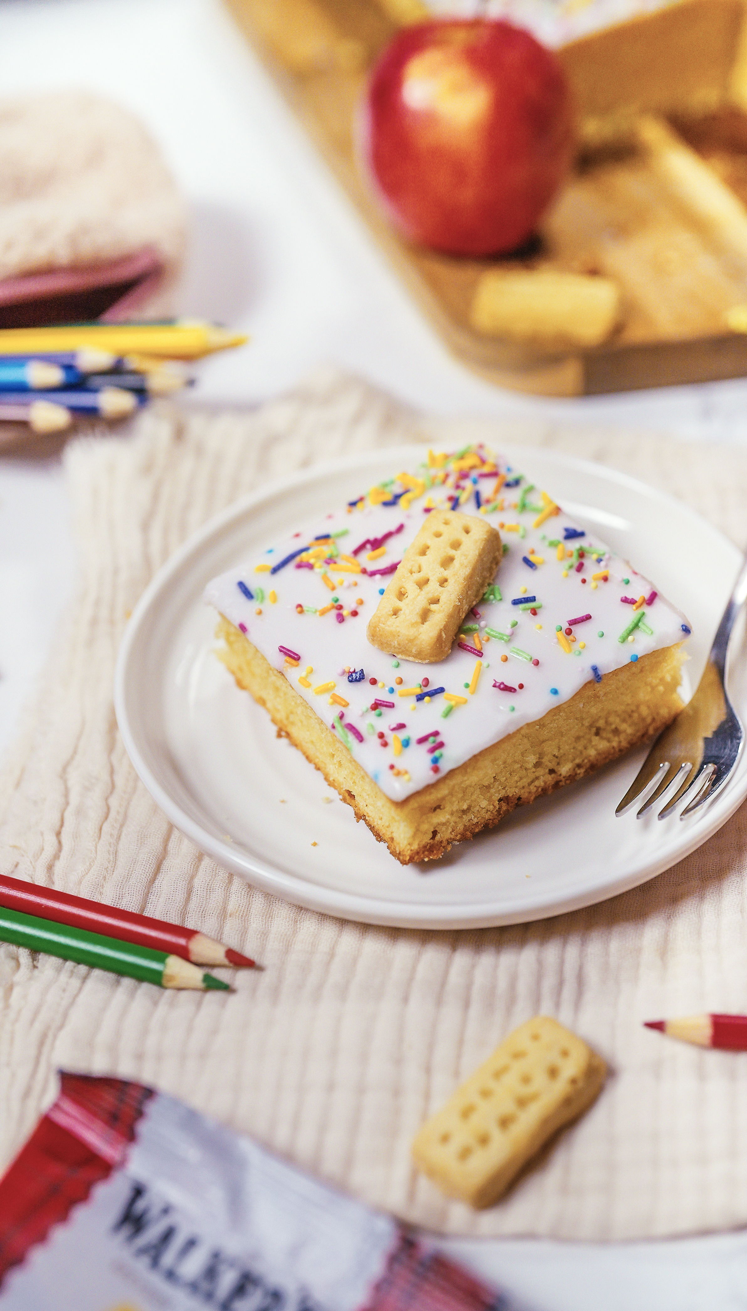 A slice of cake with frosting, sprinkles, and a biscuit on a plate.