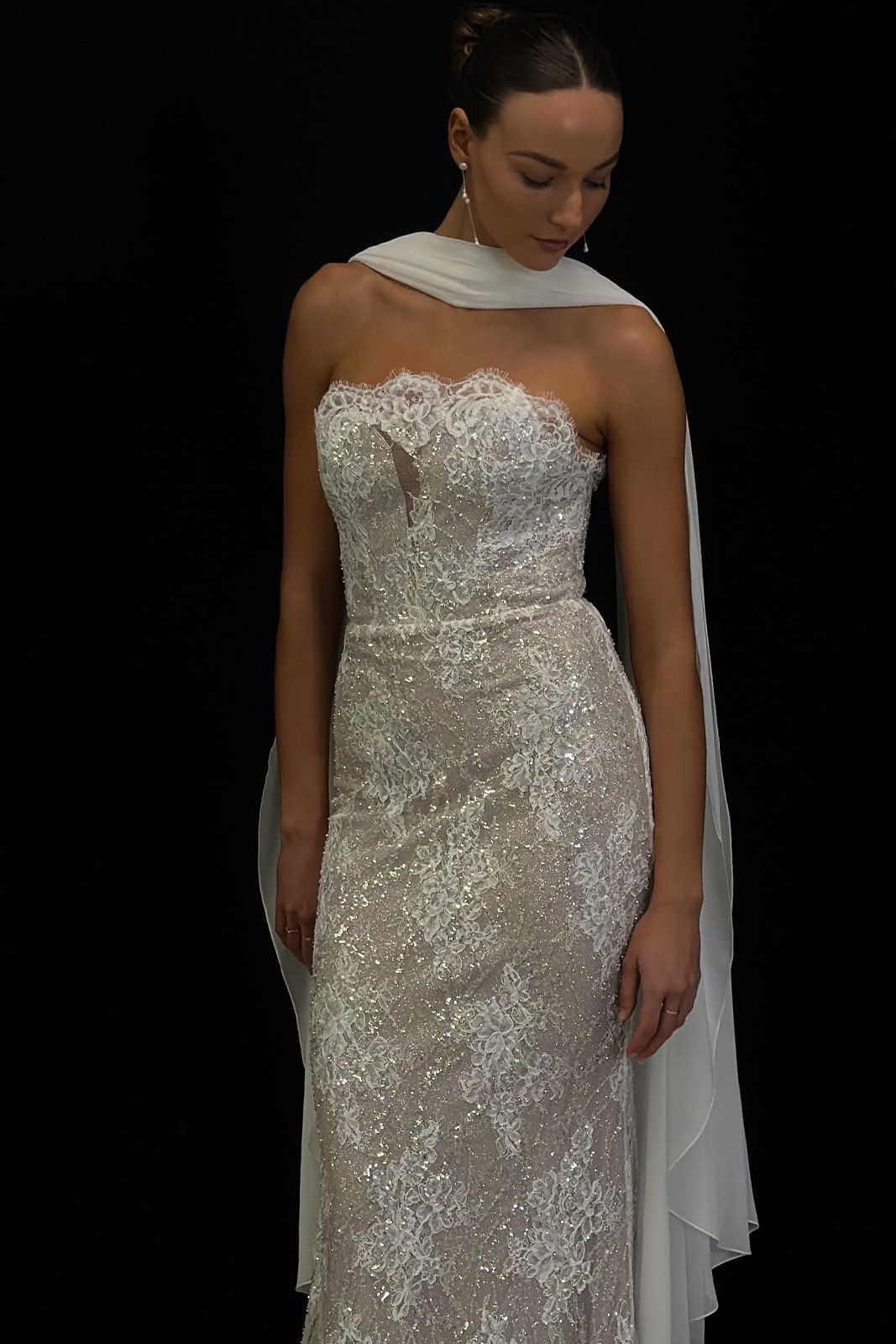 Woman in a strapless lace gown with a flowing white scarf.