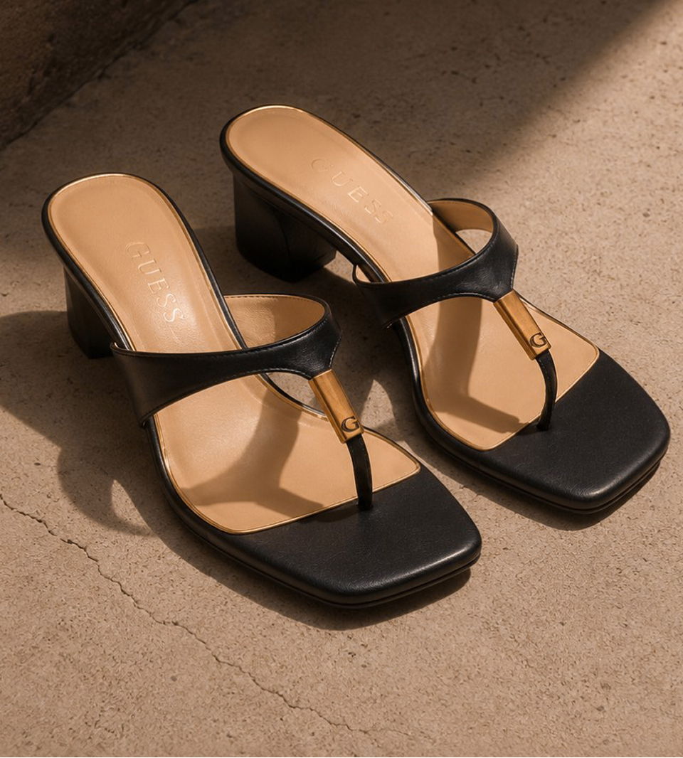 Black heeled sandals with a simple strap design on a textured surface.