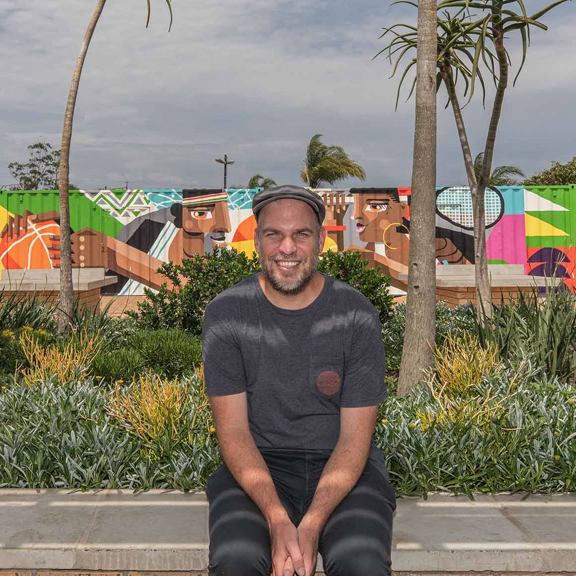 A photo of Wesley van Eden in front of a mural surrounded by palm trees.