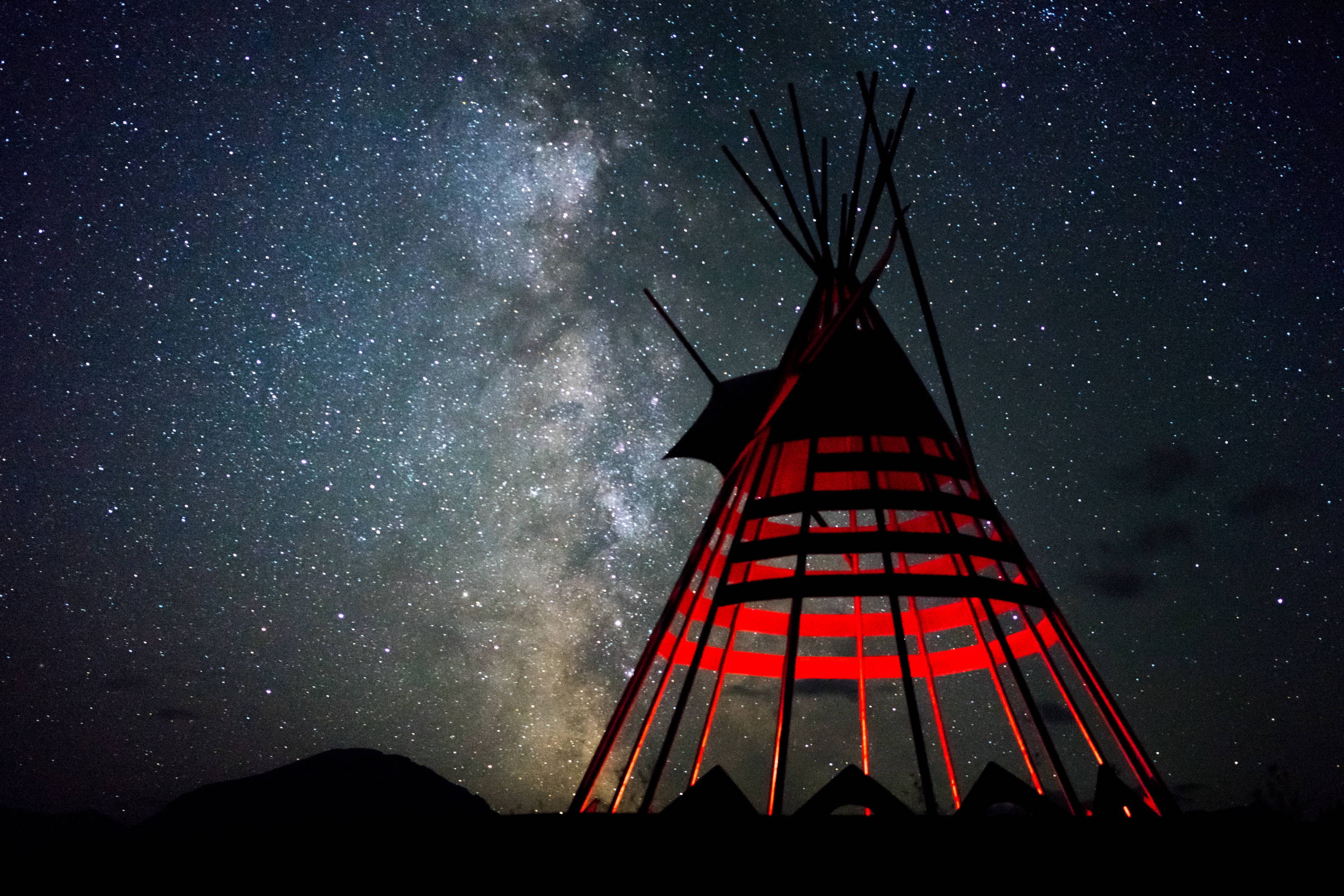 Bozeman Hot Springs & 11 Things to Do Beyond. Tee-pee without canvas displays internal light as stars in night sky shine above.
