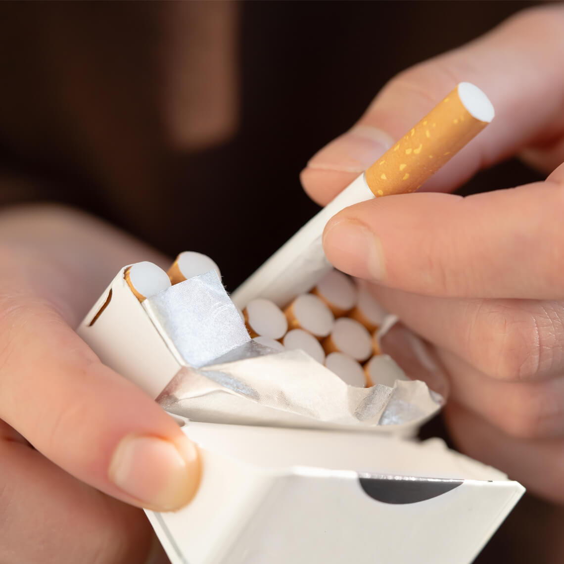 A person holding a cigarette pack with one cigarette being taken out.