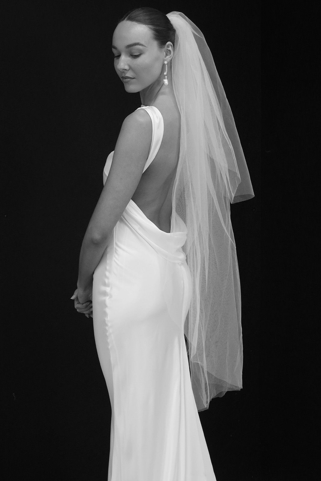 Bride in elegant white gown, showcasing a backless design and flowing veil.