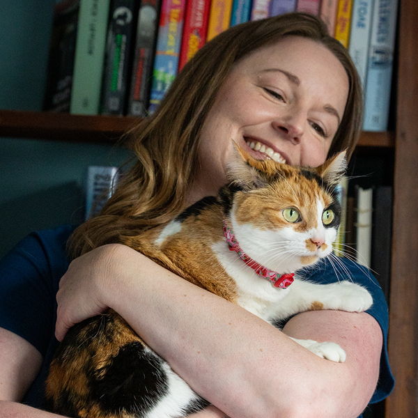 A person happily holding a calico cat in a cozy setting.