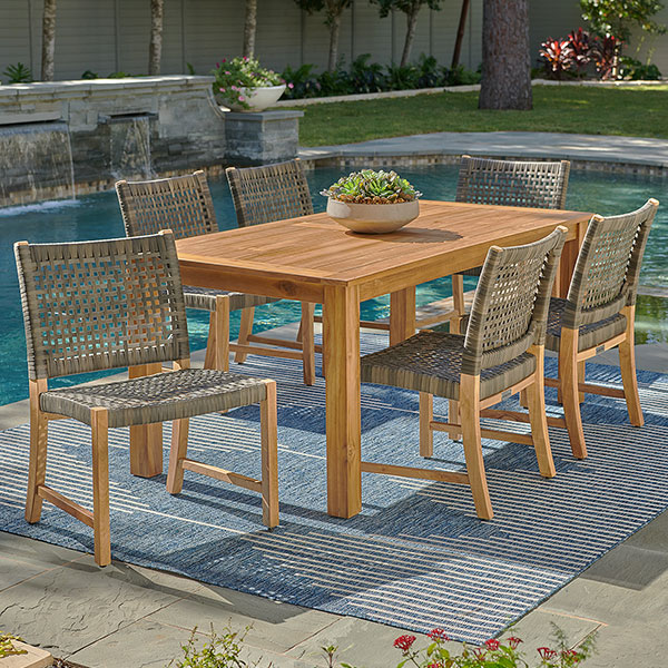 Outdoor dining set with wooden table and woven chairs by a pool.