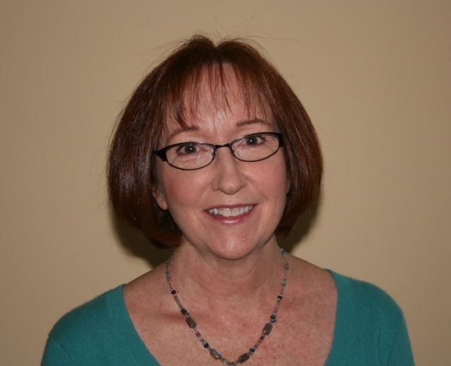 Woman with short brown hair and glasses smiling against a beige background.