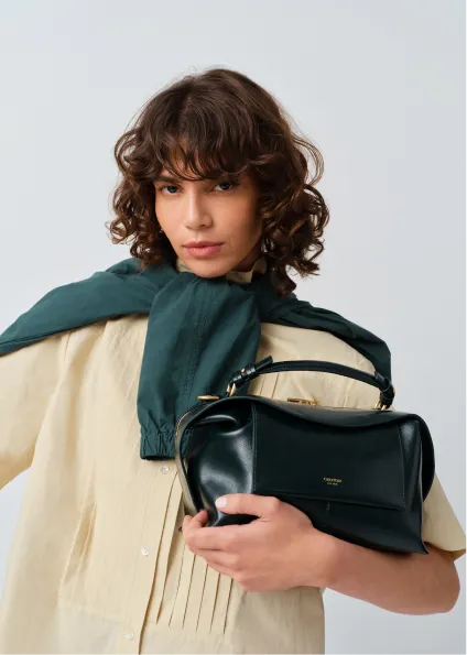 A woman with curly hair holding a black handbag, wearing a light outfit.