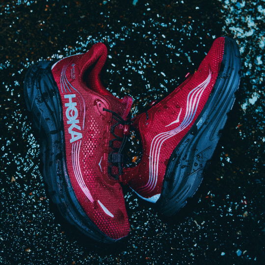 A pair of red Hoka running shoes on a dark surface.