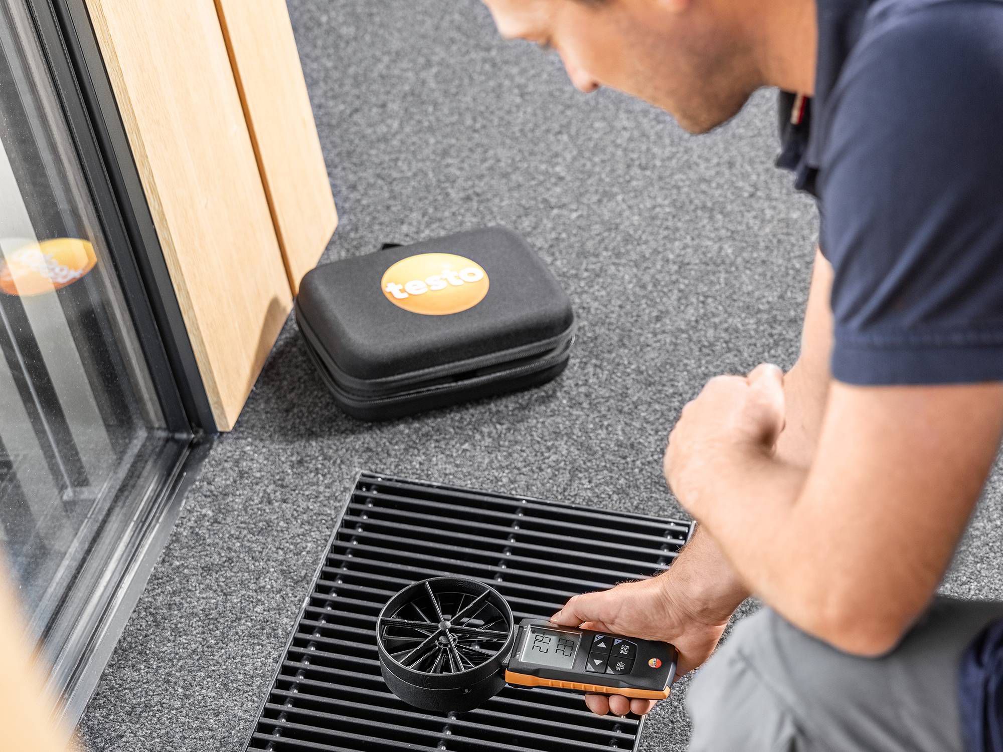 Person measuring air flow with a device near a floor vent.
