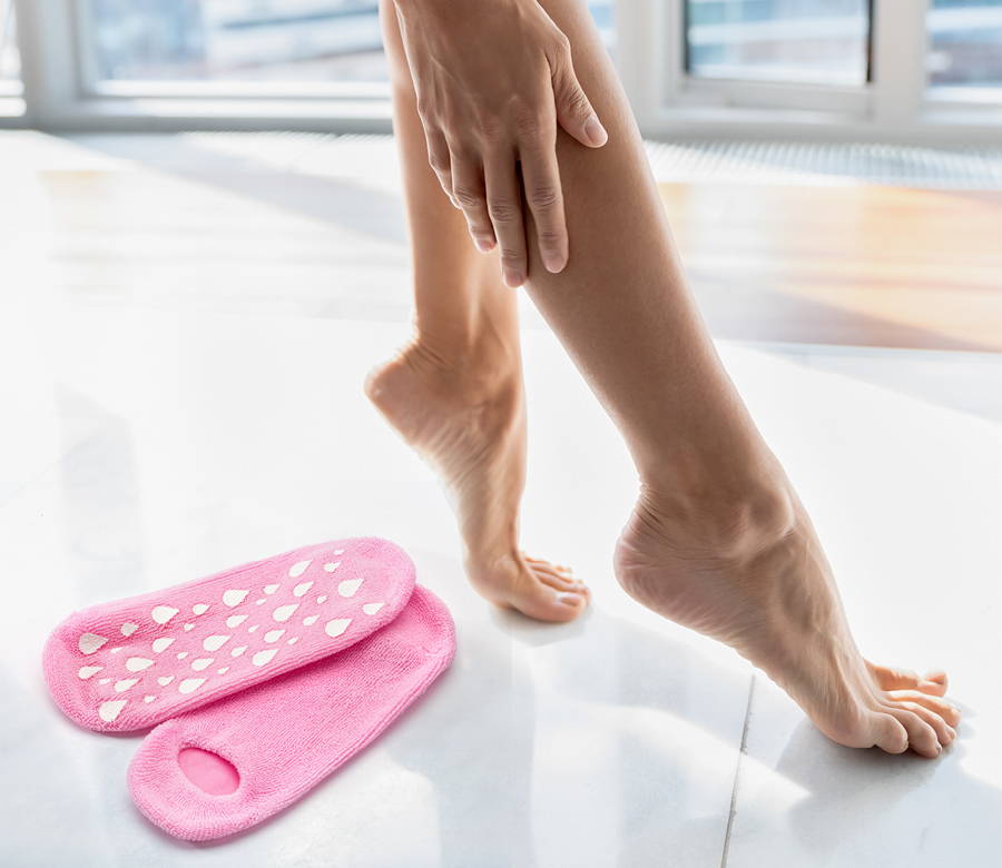 a woman touching her right calf in bare feet with hydrating socks next to her on the ground