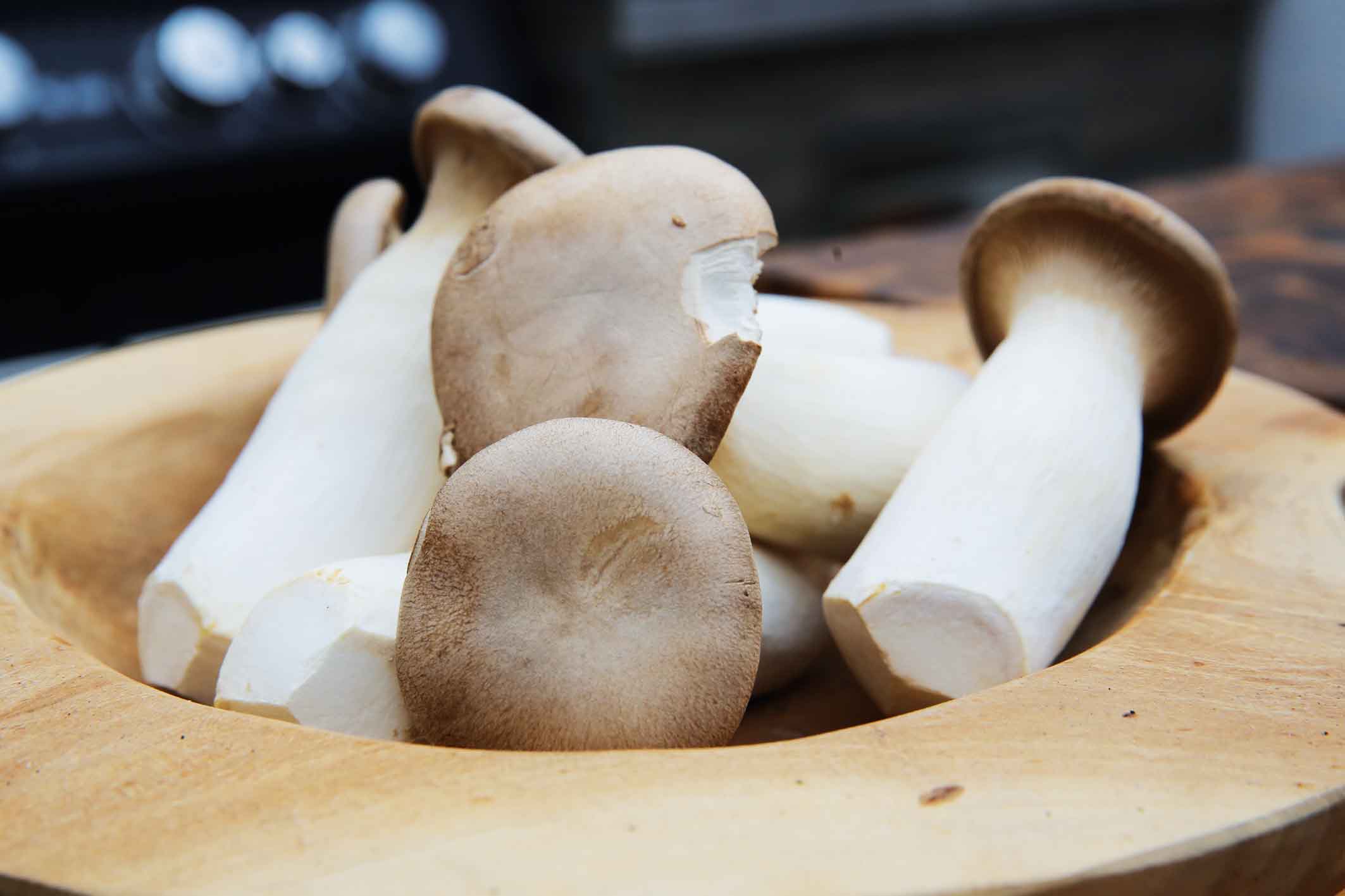 A wooden bowl containing various mushrooms.