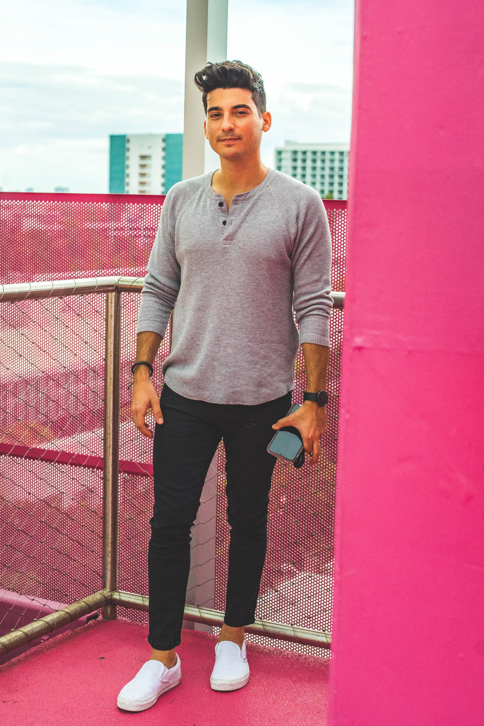 Man standing on pink porch wearing a gray henley, white shoes, and black stretch jeans from under510.com