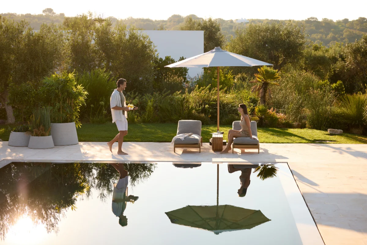 Poolside lounge chairs shaded by a large patio umbrella in a landscaped backyard, illustrating how movable shade creates comfortable outdoor relaxation areas.