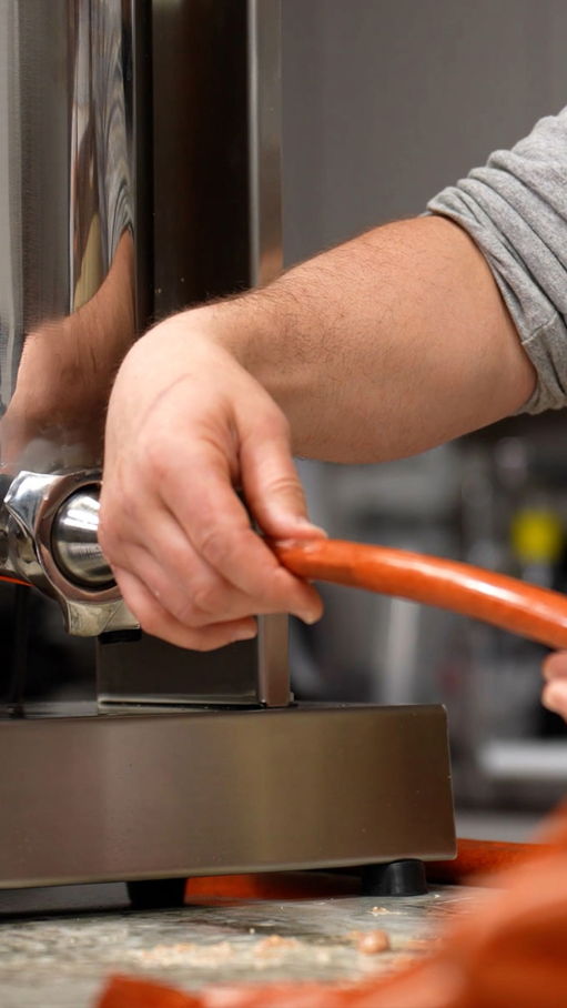Person's hand holding a sausage near a meat grinder.
