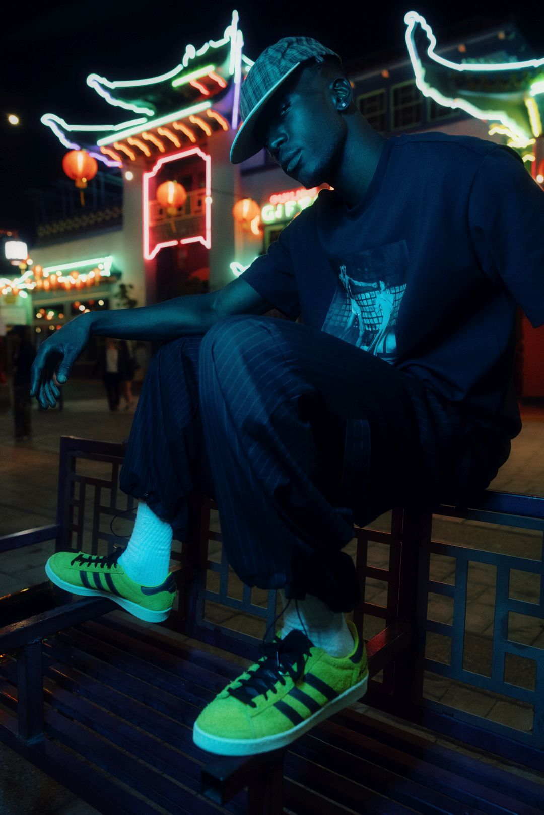 Person sitting on a bench wearing a black shirt and bright sneakers at night.