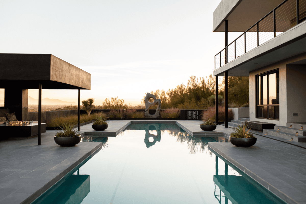 Contemporary Arizona pool courtyard with large-format pavers, minimal planting, and covered patio structure at dusk.
