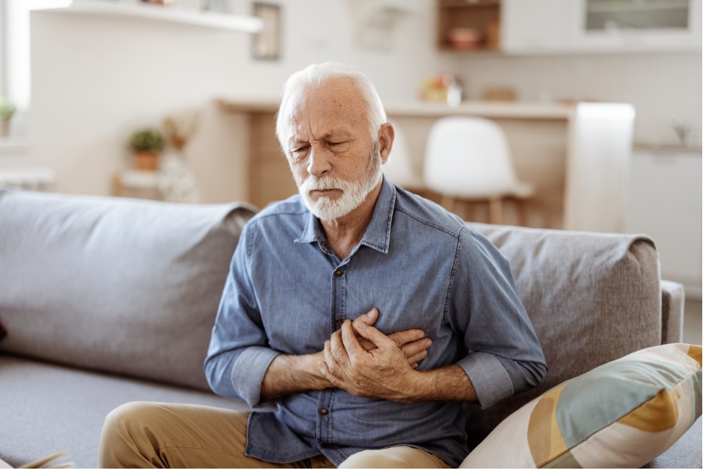 Elderly man sitting on a sofa, experiencing chest pain.