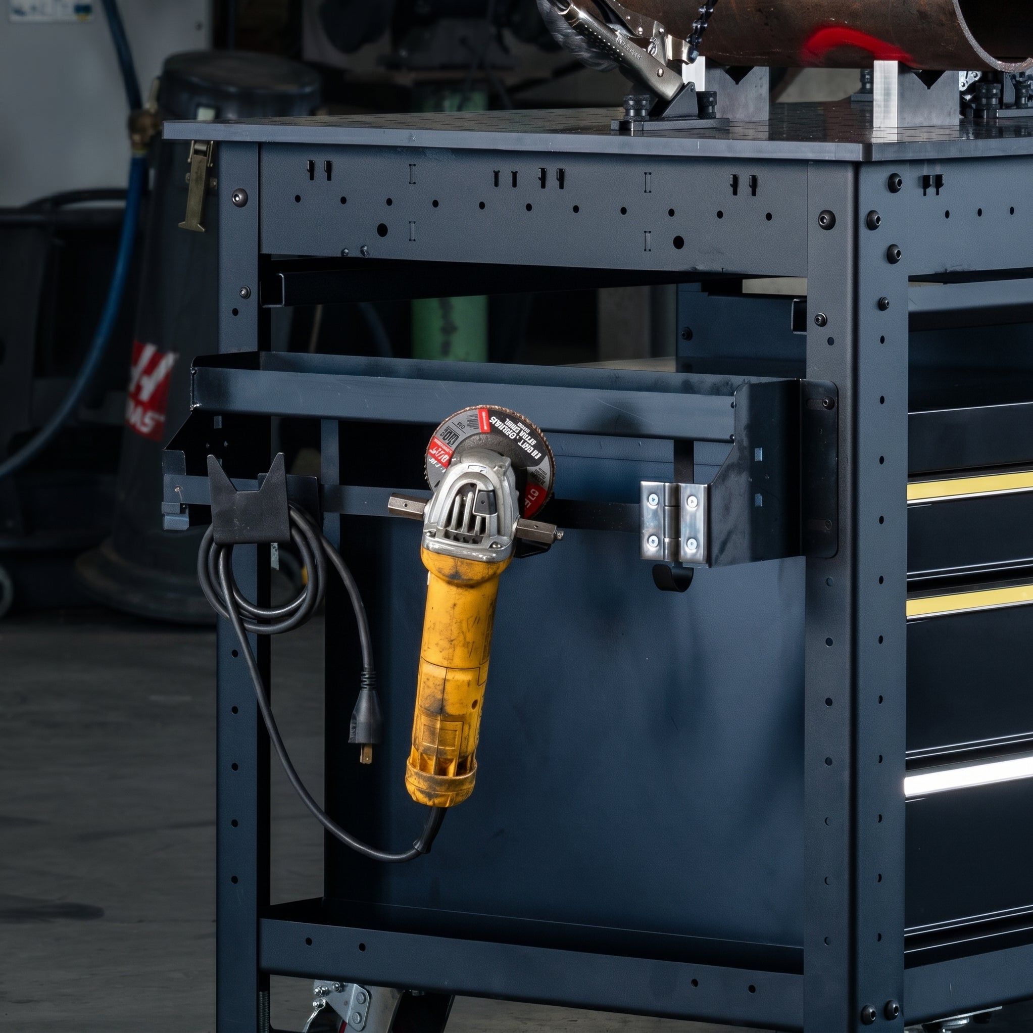A yellow power tool hanging from a black tool cart drawer.