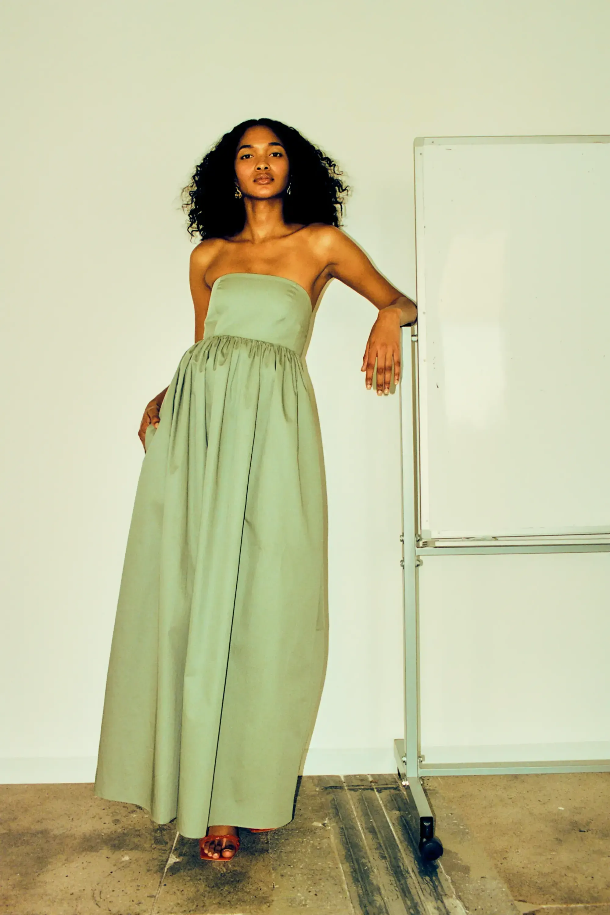 Woman wearing a strapless green gown, standing next to a whiteboard.