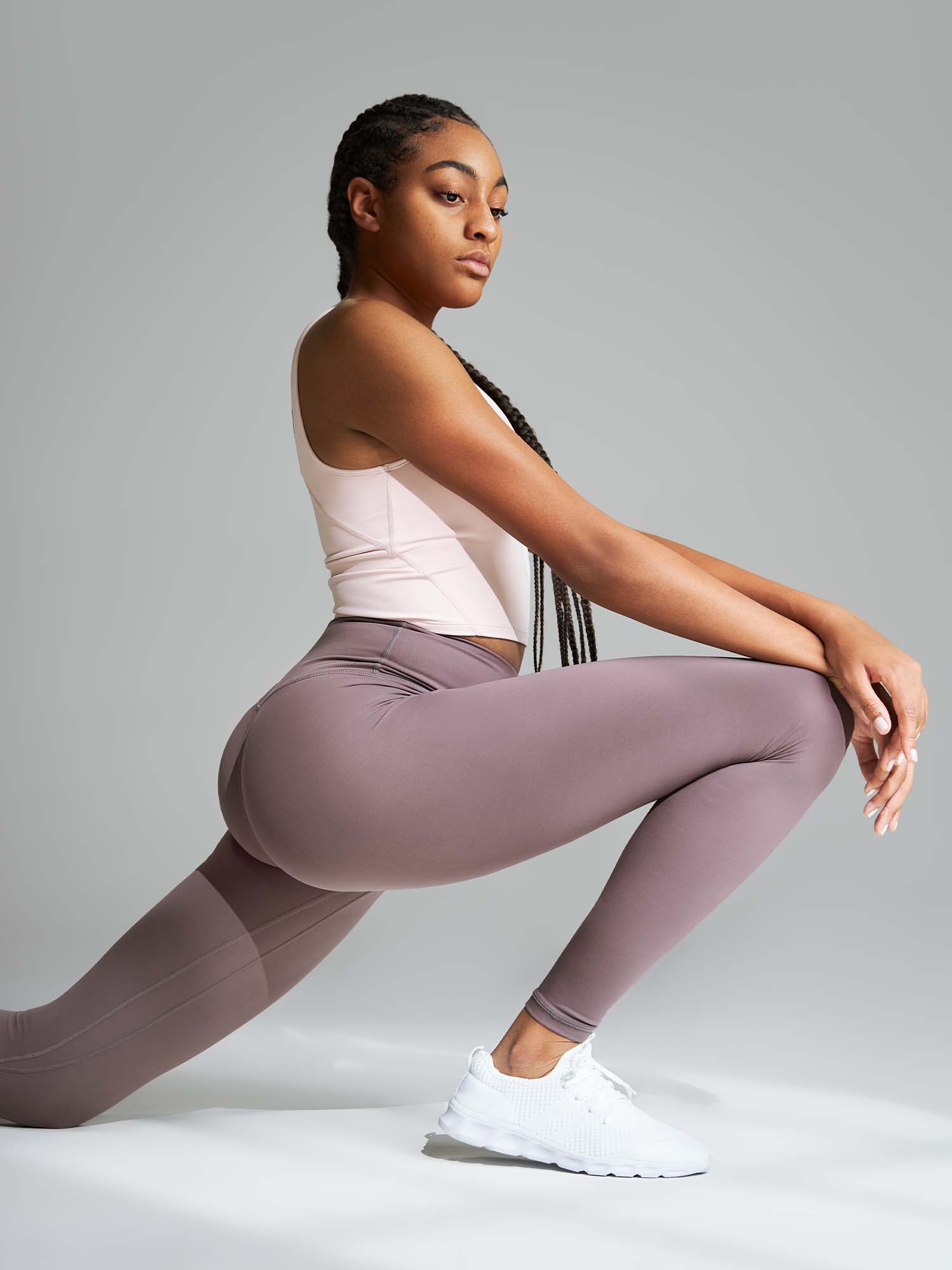 Tall woman wearing a light pink tank top and mauve leggings doing a lunge