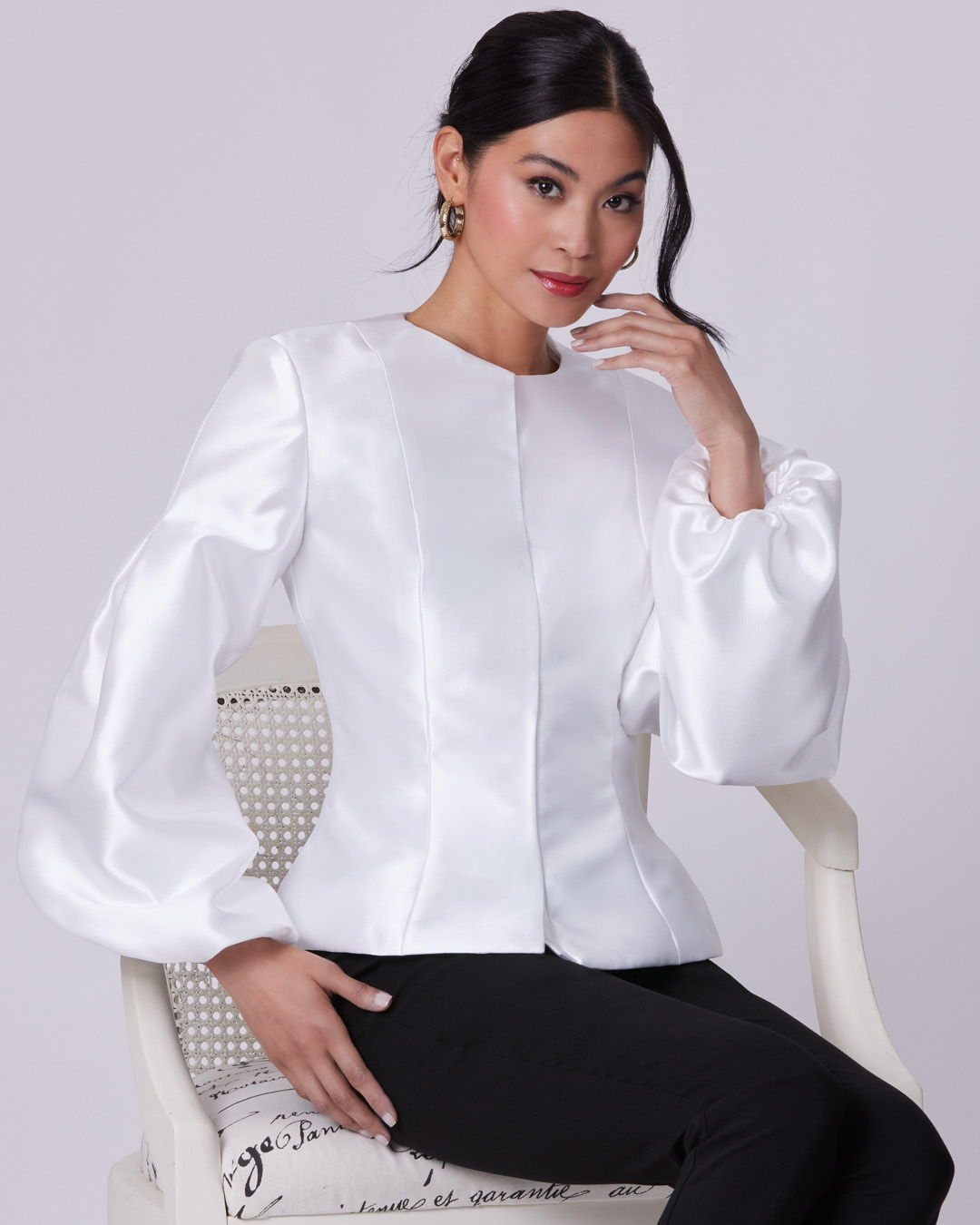 Woman in a white blouse sitting elegantly on a chair.