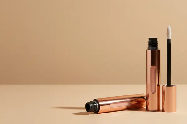Two rose gold tubes of Urban Retreat lip gloss on a beige background.