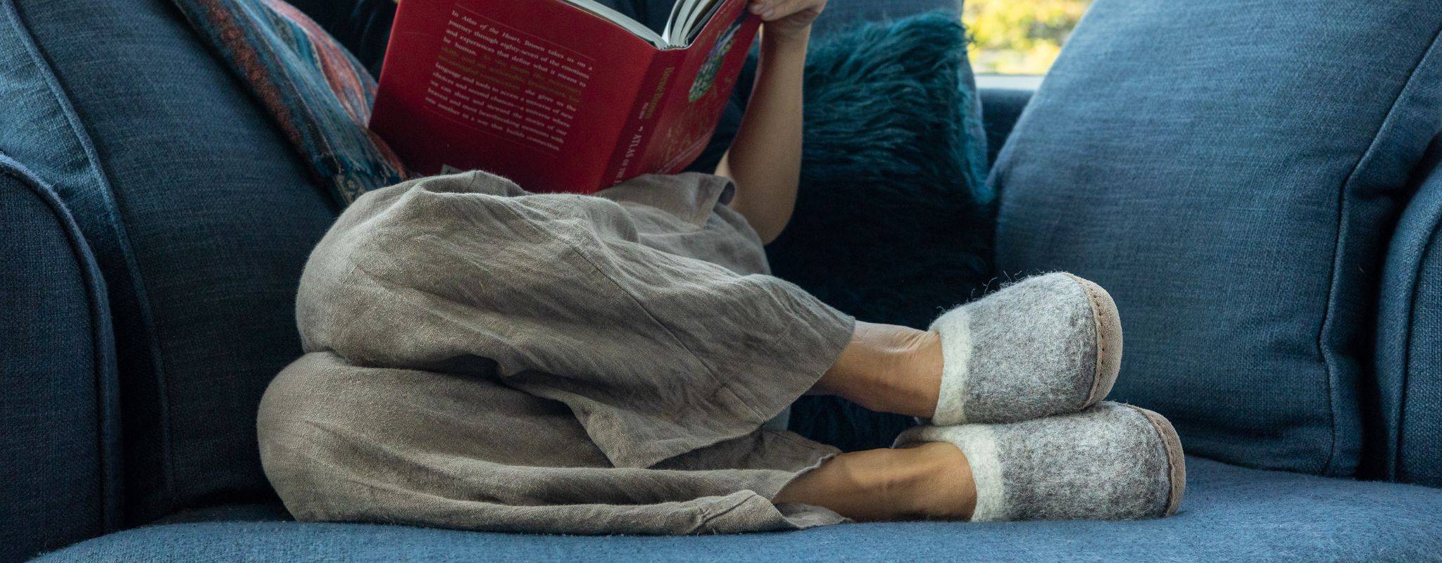 Person relaxing on a couch, reading a book, with wool slippers on their feet
