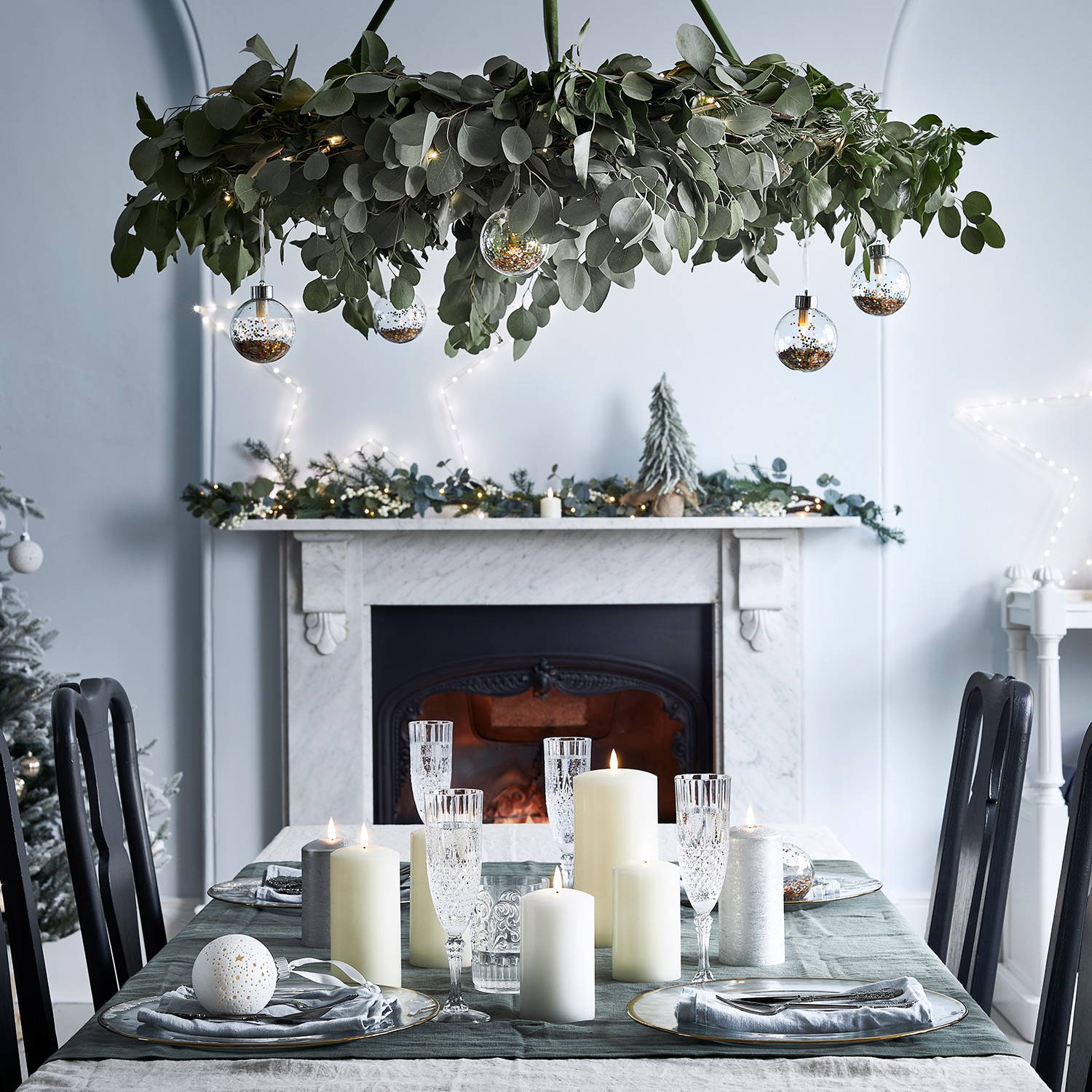 Dining room setting with festive foliage and bauble hanging feature above dining table with garland, mini tree, candles and star lights displayed
