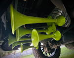 Side undercarriage view of lime green multi-bell train horns mounted on matching green bracket under truck