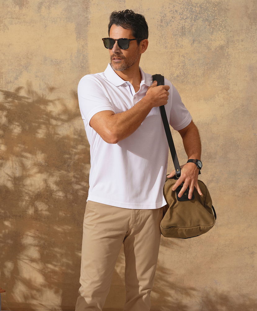 Man in sunglasses holding a bag against a textured background.