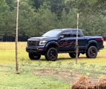 Front three-quarter lifted dark blue Nissan Titan red flame door decals off-road wheels grassy field Jonathan's Outlaw 228H gallery photo 2