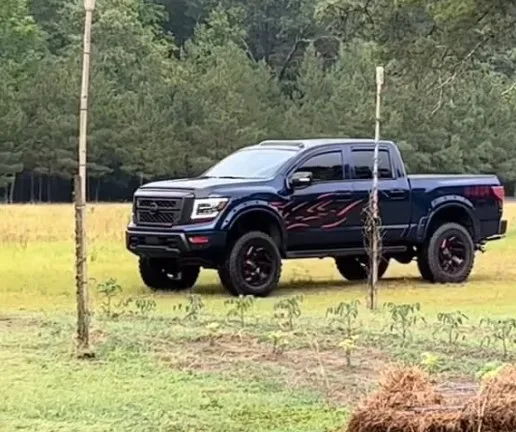 Front three-quarter lifted dark blue Nissan Titan red flame door decals off-road wheels grassy field Jonathan's Outlaw 228H gallery photo 2