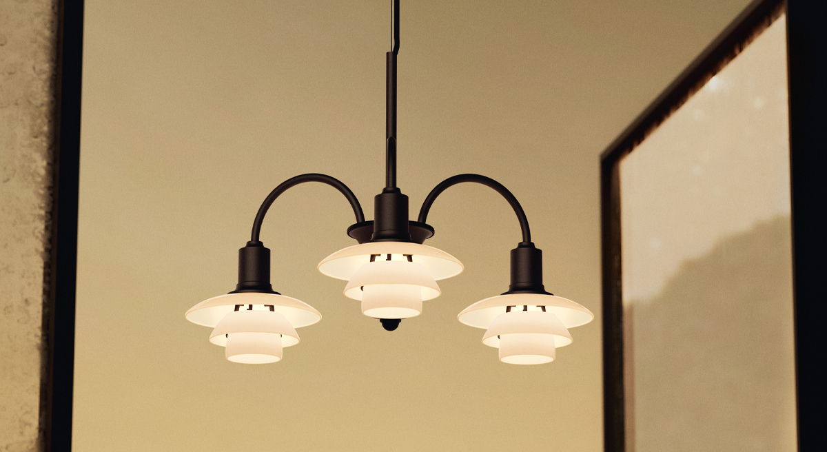 A black chandelier with three glass shades against a warm background.