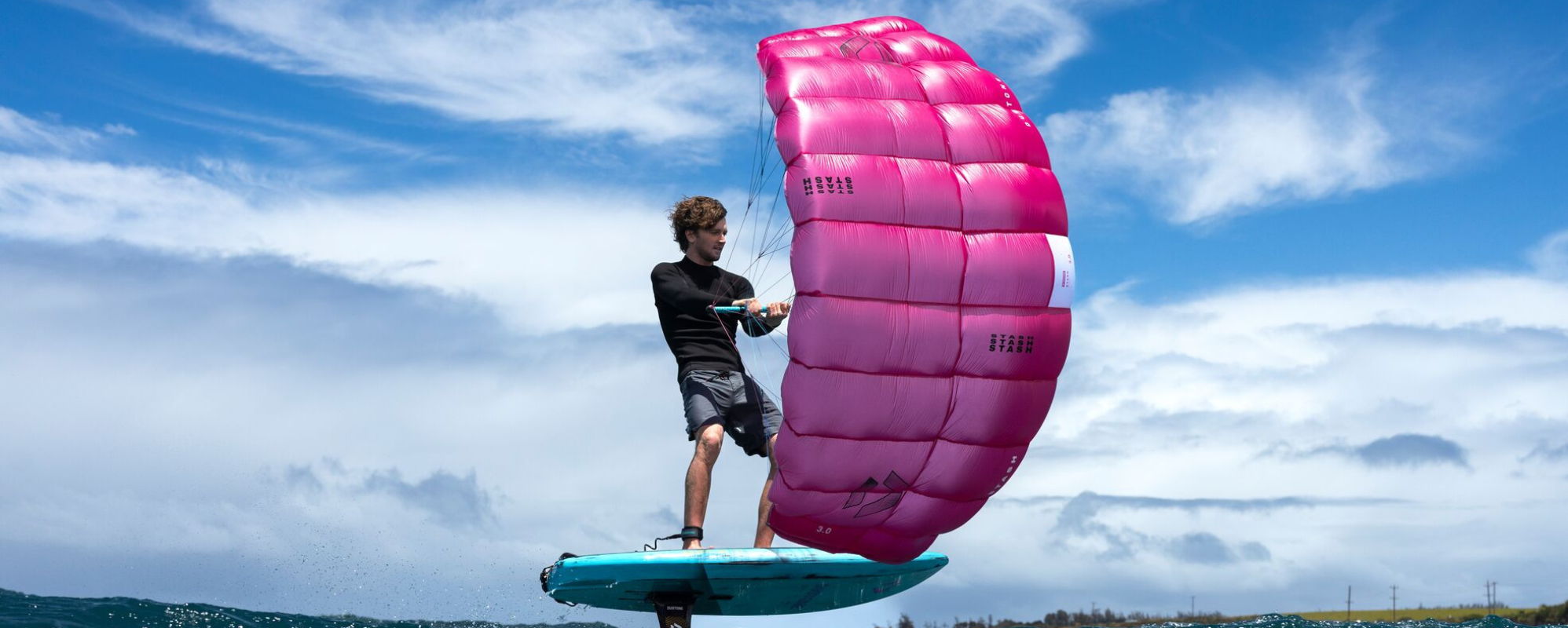 Person parawing on a colorful wing above water under a blue sky.