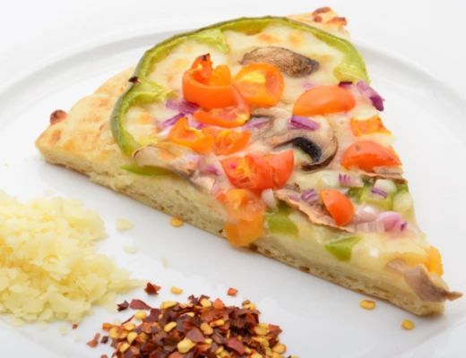 A slice of vegetable pizza with toppings and side condiments.