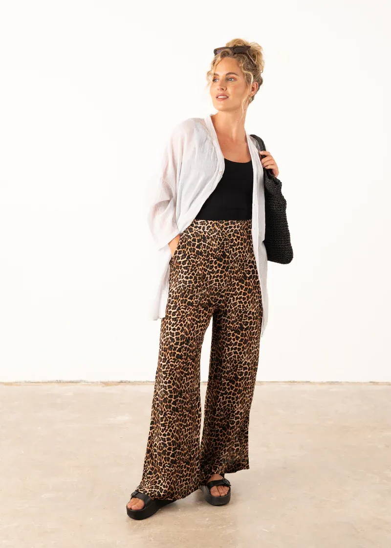 A model wearing a pair of leopard print, wide leg trousers with a black tank top, white overszied shirt and black platform slides