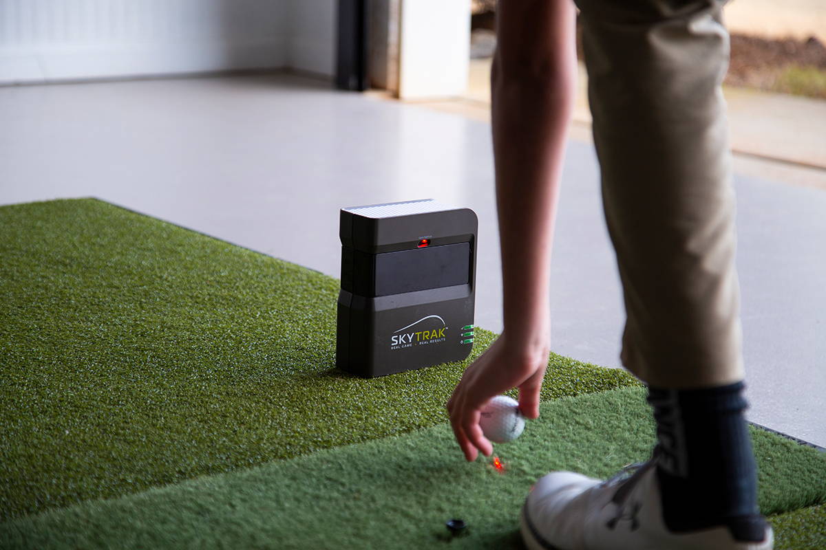 A SkyTrak golf launch monitor and simulator unit and someone setting a golf ball in front of it