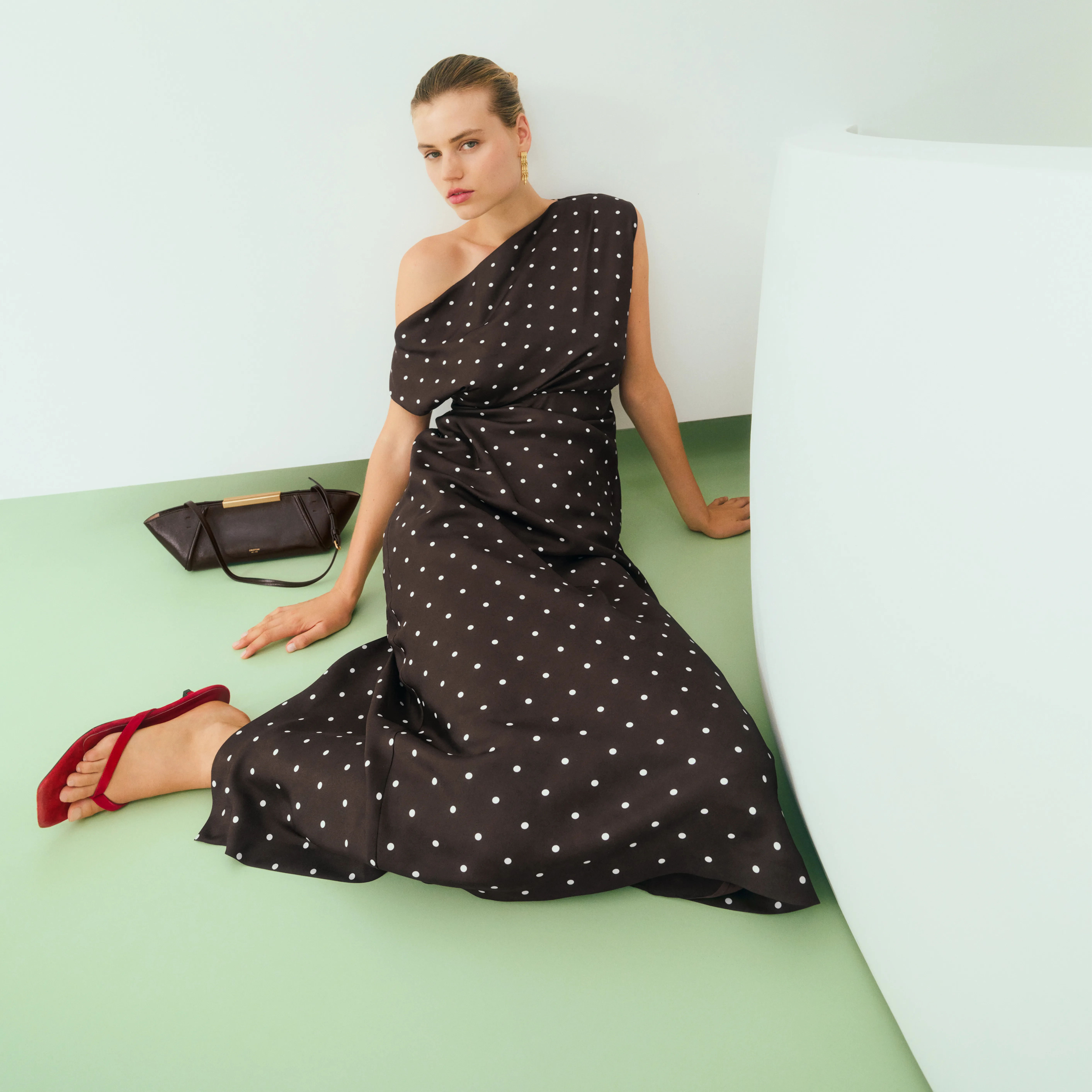 Model in a polka dot dress sitting against a white wall.