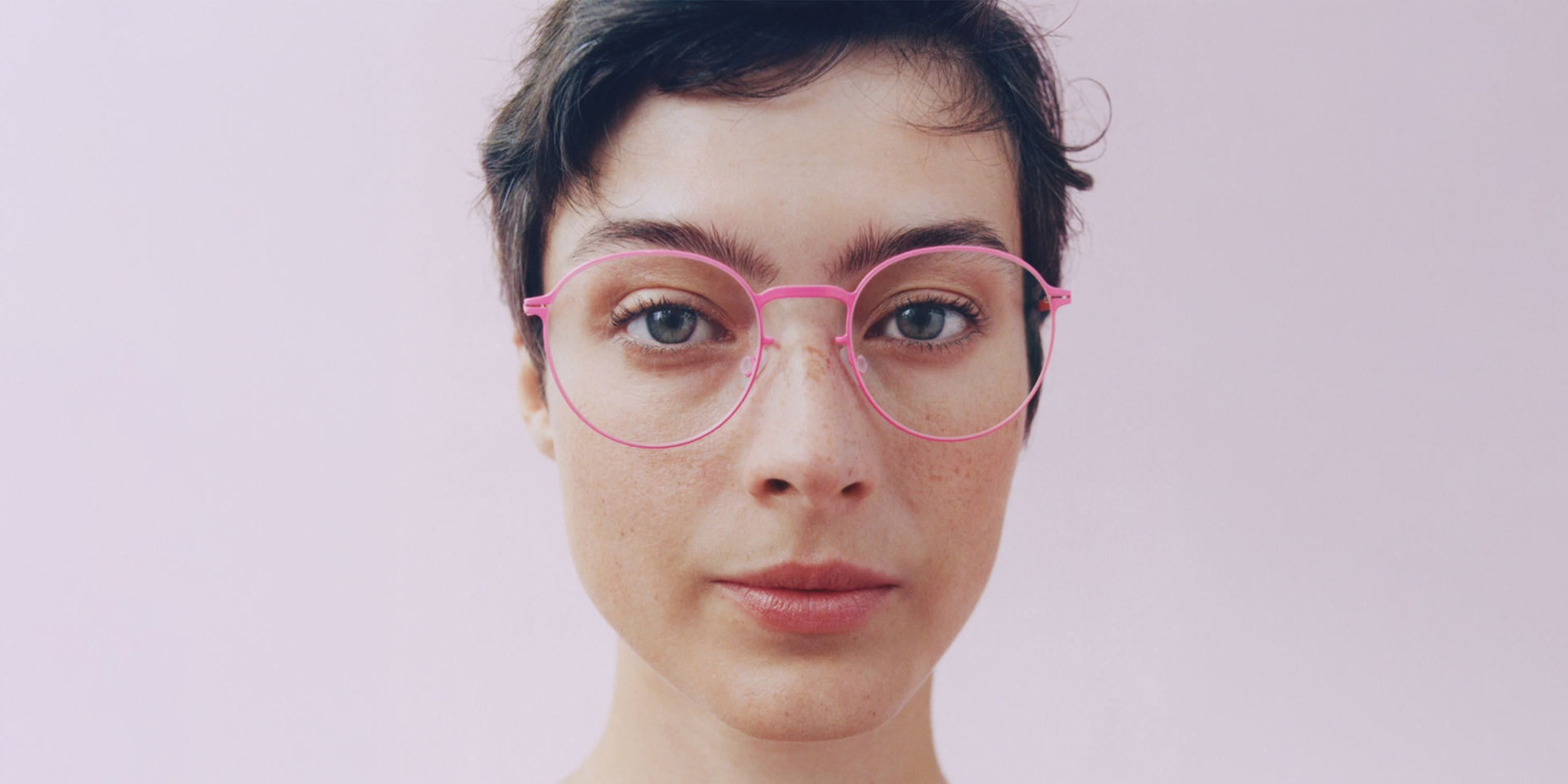 Person with short hair wearing pink Mykita glasses against a pink background.