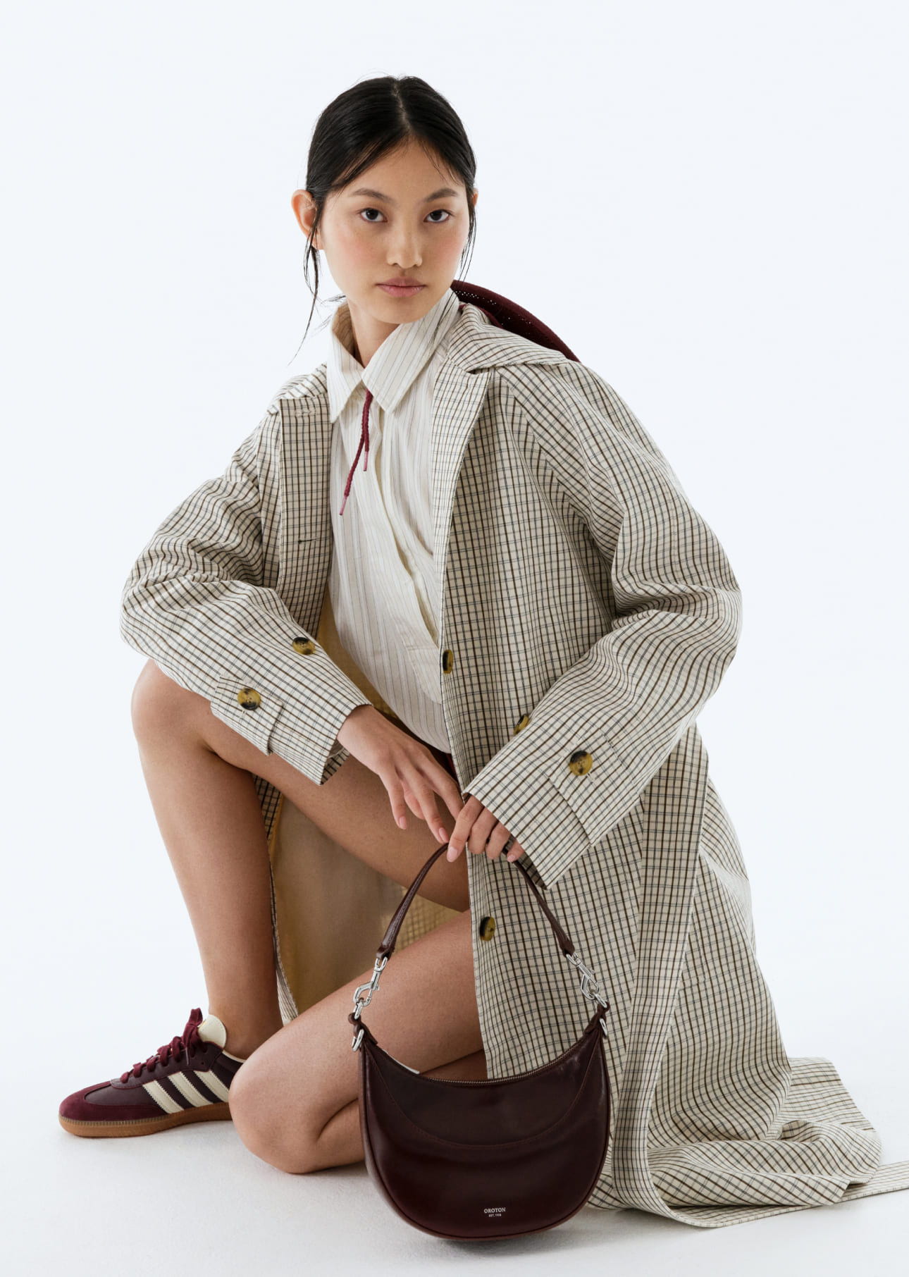 Model wearing a coat, white shirt, and holding a handbag.