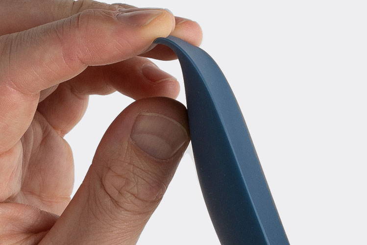 A hand bends the edge of a blue Misen Spoontula to demonstrate its flexibility.