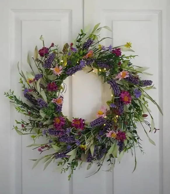 The lavender wreath hung on a white door with warm white micro lights.